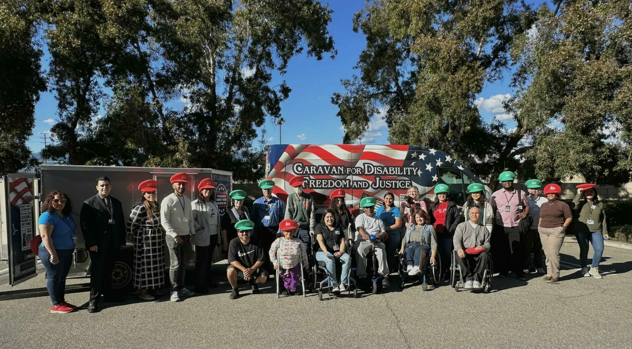 A large group photo of Rolling Start staff, board members, partners, and consumers posing together wearing Latanya Reeves hats with the Caravan for Disability Freedom and Justice van in the background
